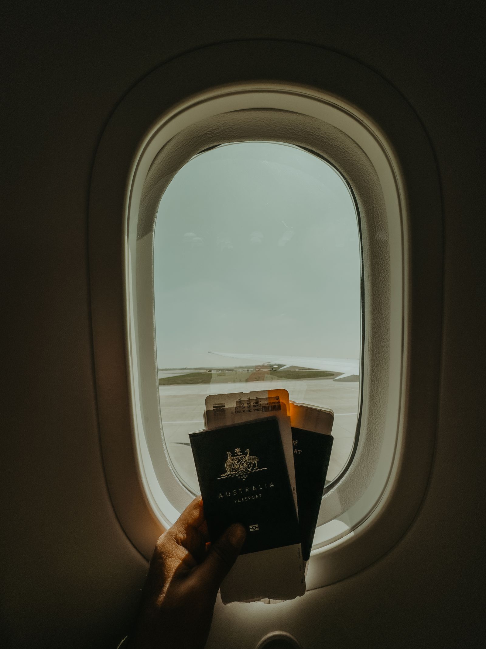 Hand holding a passport and boarding pass by an airplane window, representing travel planning for an Ayurvedic trip