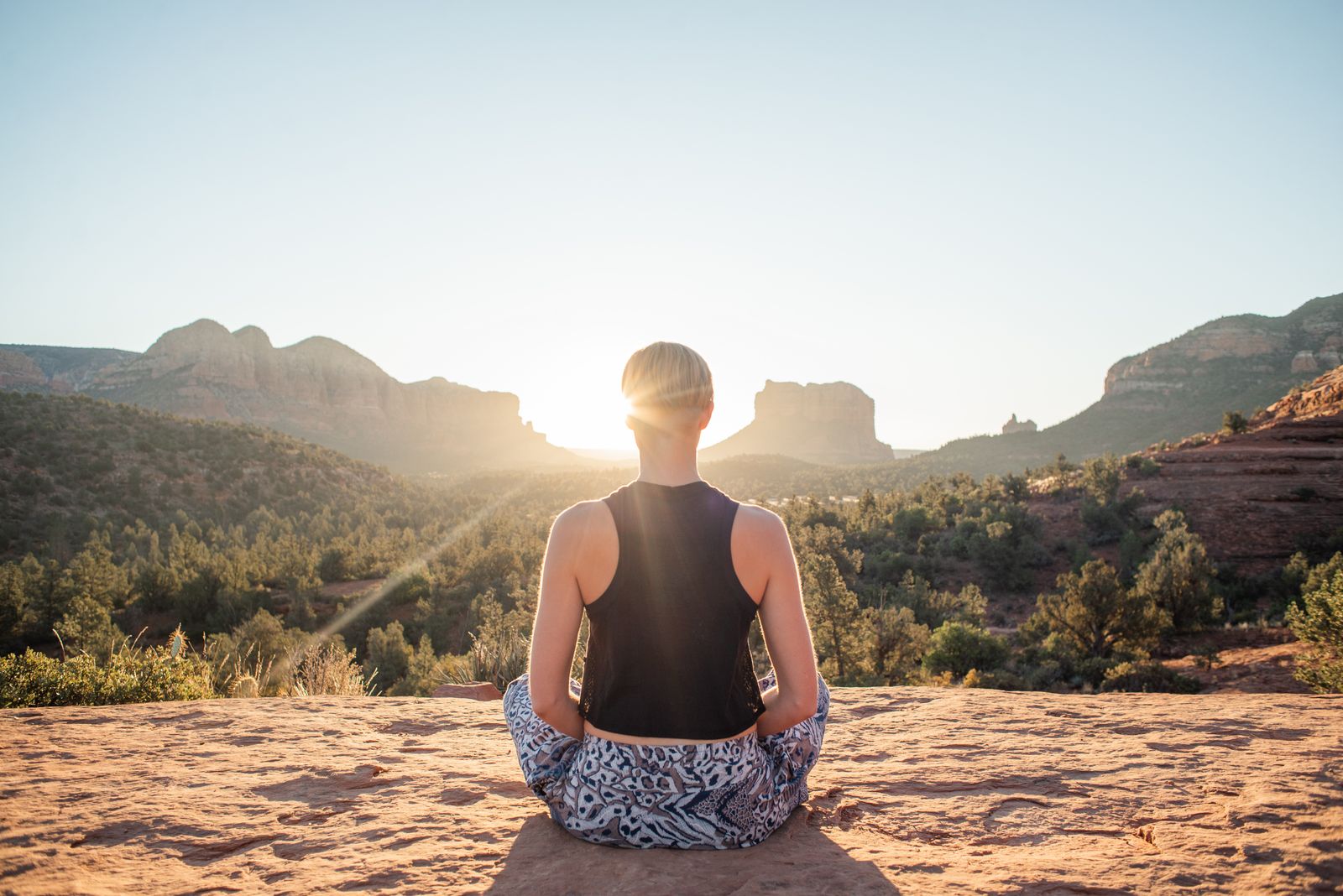 Woman in a meditative lotus position on a sunlit cliff at sunrise, representing Ayurvedic daily routine